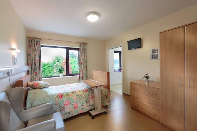A resident bedroom at Norwood Grange with a bed, wardrobe, chest of drawers, armchair and a window onto the garden