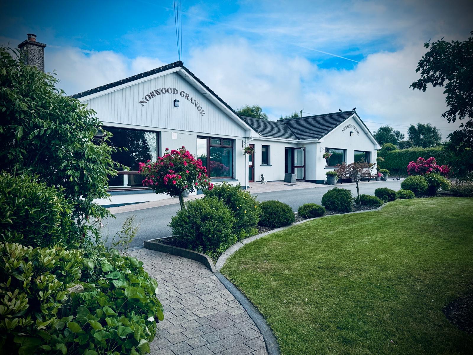 The front of Norwood Grange Nursing Home, a white single-storey building with lawns and rose bushes